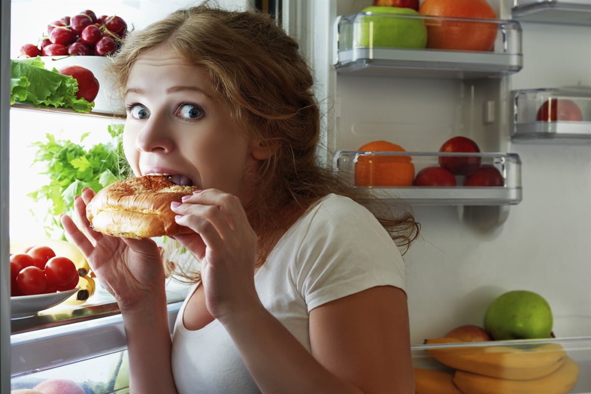 woman eats sweets at night to sneak in a refrigerator